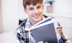 Uśmiechnięty student z książkami, zastanawia się, jak rozliczyć dochody dziecka pełnoletniego uczącego się.