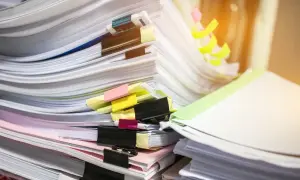 Stosy dokumentów, wśród nich duplikat świadectwa pracy, z kolorowymi zakładkami i spinaczami.