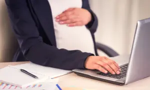Kobieta w ciąży przygotowuje wniosek o urlop macierzyński, pracując przy laptopie.