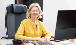 Uśmiechnięta wicedyrektor w żółtej bluzce siedzi przy biurku, gotowa do pracy.