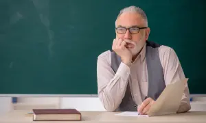 Starszy nauczyciel zamyślony nad dokumentami, być może planuje swoją sześciomiesięczną odprawę emerytalną.
