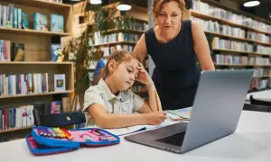 Dziewczynka z ołówkiem w dłoni, zamyślona nad zadaniem, przygotowuje podanie do szkoły średniej. Nauczycielka wspiera ją w bibliotece.