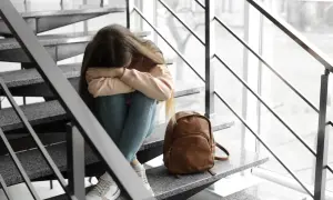 Smutna dziewczyna siedzi na schodach, przytulając kolana. Obok niej leży plecak. Martwi się o warunkowe przejście do następnej klasy.