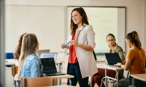 Nauczycielka wita studentów, omawiając jak zostać nauczycielem. W sali lekcyjnej panuje atmosfera nauki i zaangażowania.