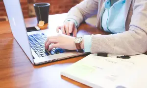 Osoba pracuje na laptopie, studiując różne rodzaje wykształcenia. Na biurku leży notatnik i kubek z herbatą.