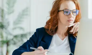Kobieta w okularach z modną oprawką pracuje przy laptopie. Dofinansowanie do okularów może pomóc w zakupie stylowych i wygodnych oprawek.