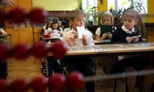 Dzieci siedzą w ławkach, ucząc się, kiedy idą do szkoły. Jedna dziewczynka trzyma kartę z cyfrą.