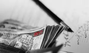 Stos banknotów 100 zł w portfelu, obok pióro i zapiski. FGŚP.