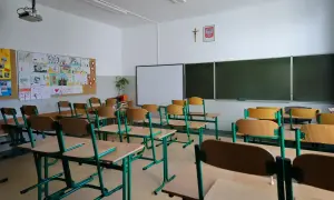 Pusta klasa szkolna z rzędami ławek i krzeseł. Na ścianie tablica, projektor i dziecięce rysunki. Cisza i spokój, jakby odwołane zajęcia w szkołach.
