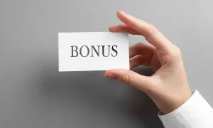 Dłoń trzyma kartkę z napisem "BONUS". To może być zapowiedź dodatku stażowego, który czeka na pracownika.