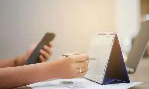 Ręka z długopisem zaznacza datę w kalendarzu, sprawdzając, czy 1 listopada jest dniem wolnym od pracy. Obok leży telefon.