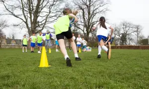 Dzieci w strojach sportowych biegają po trawie, ćwicząc. Może to być inspiracja, jak napisać zwolnienie z wf, gdy dziecko jest chore.
