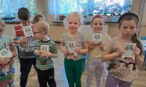 Dzieci z oddziału przedszkolnego świętują Dzień Ziemi, trzymając w rękach kartki z motywem planety i słodkości.