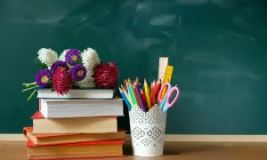 Kwiaty na stosie książek i przybory szkolne na tle zielonej tablicy. Idealna kompozycja na Dzień Edukacji Narodowej.