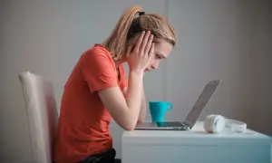 Zmartwiona dziewczyna z rękami na skroniach patrzy na laptopa. Może to być związane z zawieszeniem w prawach ucznia.