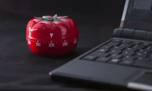 Czerwony minutnik w kształcie pomidora obok klawiatury laptopa, gotowy do pracy metodą pomodoro.