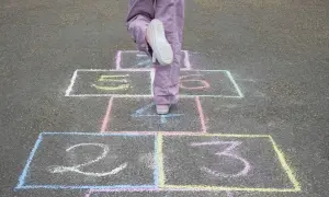 Dziecko skacze w gra w klasy. Kolorowe pola z cyframi 1, 2, 3, 5, 6 namalowane kredą na asfalcie.