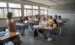 Nauczycielka prowadzi lekcję, a uczniowie siedzą w ławkach, słuchając jej uważnie. Wszyscy są zaangażowani w proces nauczania, a atmosfera jest pełna skupienia.