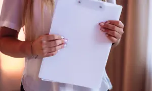 Kobieta w białej bluzce trzyma białą teczkę. To przykład opinii mentora o nauczycielu, która może być pozytywna lub negatywna.