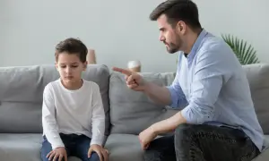 Ojciec karci syna, który siedzi ze spuszczoną głową. Chłopiec wygląda na przygnębionego, jakby doświadczał efektu Golema, czując się niekompetentny.