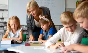 Nauczycielka, jak dobra oligofrenopedagog, wspiera dzieci w nauce przy stolikach.