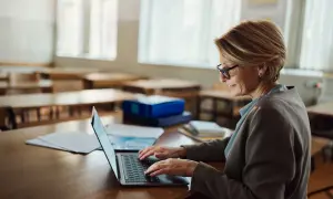Kobieta w okularach pracuje na laptopie w pustej sali lekcyjnej. Może szukać informacji o studiach podyplomowych online bezpłatnych.