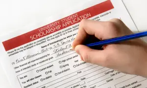 Ręka wypełnia wniosek o stypendium szkolne. Aplikacja o stypendium uniwersyteckie jest w trakcie wypełniania.
