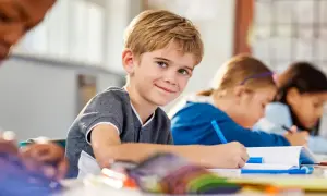 Uśmiechnięty chłopiec z blond włosami siedzi w klasie, pisząc w zeszycie. To jego nowy przedmiot w szkole, a on jest podekscytowany nauką.