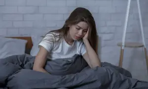 Młoda kobieta w łóżku, z ręką na twarzy, przeżywa trudne chwile, być może **ataki paniki**.