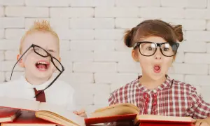Dzieci z okularami i książkami, wesołe i zaskoczone. Wczesna pedagogika w praktyce, rozbudzająca ciekawość świata.