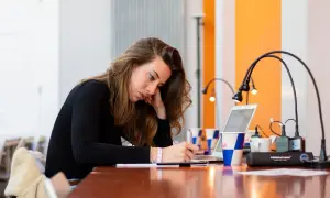 Młoda kobieta pochylona nad notatkami, szukająca sposobów, jak się lepiej uczyć. Obok laptop i kubek z logo Red Bull.