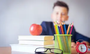 Chłopiec z fobią szkolną patrzy na stos książek, jabłko i kolorowe kredki. Zegar tyka, odmierzając czas do lekcji.