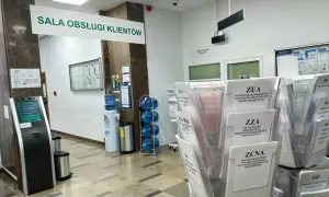 W sali obsługi klienta ZUS, obok dystrybutora wody, stoją stojaki z formularzami, m.in. ZUA, ZZA, ZCNA, RCA, ZUS RSA.