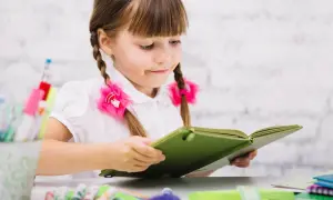 Dziewczynka z warkoczami czyta książkę, marząc o przyszłości, gdy zdobędzie kurs pedagogiczny uprawniający do pracy w szkole.