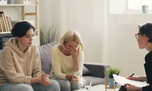 Rodzina na sesji u psychologa. Matka płacze, syn siedzi obok. Rozmowa o tym, ile zarabia psycholog szkolny, może pomóc w zrozumieniu wyzwań.