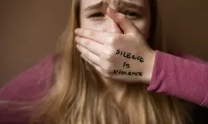 Przerażona dziewczyna zakrywa usta dłonią z napisem "Silence is violence". To obraz patologii społecznej, która odbiera głos.