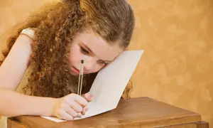 Dziewczynka z kręconymi włosami i piegami z trudem pisze, walcząc z dysleksją rozwojową.