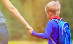 Chłopiec z plecakiem idzie za rękę z dorosłym. To może być początek przygody po rekrutacji uzupełniającej do przedszkola.