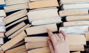 Stos książek, wśród nich cke lektury obowiązkowe. Dłoń z pierścionkiem sięga po jedną z nich.