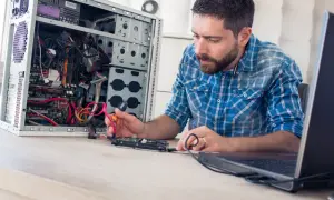 Mężczyzna, jako **technik informatyk**, naprawia komputer, podłączając dysk twardy.