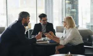 Trzy osoby przy stoliku omawiają sprawy firmy, być może związane z zfśs. Kobieta i dwaj mężczyźni w eleganckich strojach.