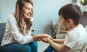 Kobieta wspiera chłopca, trzymając go za ręce. Rozmowa o wydłużeniu etapu edukacyjnego, budowanie pewności siebie.