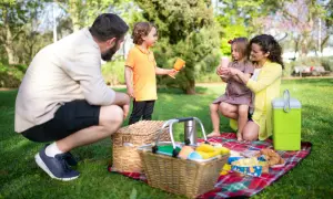 Radosny piknik rodzinny w parku. Rodzice i dzieci cieszą się wspólnym czasem na kocu, wśród zieleni.