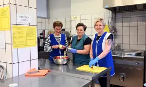 Trzy kobiety w fartuchach obierają jabłka w kuchni. Jedna z nich, intendentka, przygotowuje owoce do dalszej obróbki.