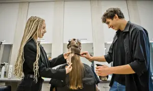 Uczniowie podczas egzaminu zawodowego fryzjer, ćwiczą cięcie włosów na modelce.