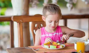 Dziewczynka je owoce, jak w przykładowy jadłospis dla dzieci w wieku 10-12 lat. Na talerzu arbuz i pomarańcza.