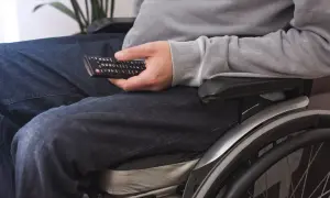 Osoba na wózku inwalidzkim, z pilotem w dłoni, doświadcza umiarkowany stopień ograniczenia ruchomości, ale nadal cieszy się rozrywką.