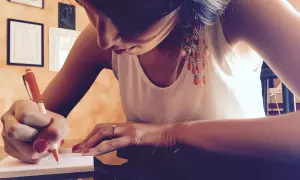 Pisze usprawiedliwienie nieobecności w szkole. Długopis w dłoni, skupiona mina, ozdobne kolczyki.