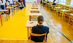 Uczniowie siedzą przy ławkach w sali gimnastycznej, przygotowując się do egzaminu dojrzałości.