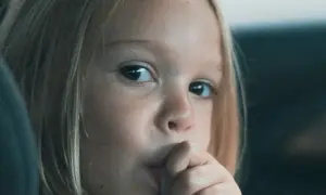 Zamyślona dziewczynka z blond włosami wkłada palec do ust. Może to być oznaka stresu lub nawyku, co na obgryzanie paznokci u dzieci warto sprawdzić.